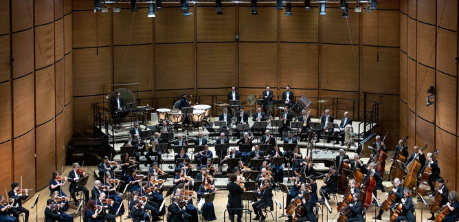 A large orchestra is playing on a stage. Many musicians in formal attire are visible, with various instruments. | © Angelica Concari