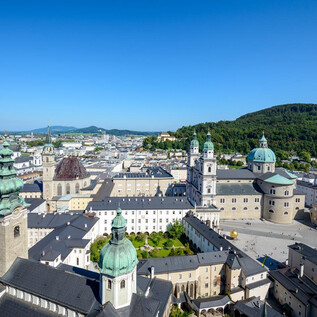 An impressive view of the city of Salzburg with historic buildings and green hills. The clear blue sky completes the picturesque image. | © Tourismus Salzburg