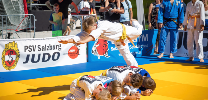 A judo demonstration on a mat with several young fighters. An athlete jumps over his training partner and showcases an impressive technique. | © Wild + Team Fotoagentur GmbH