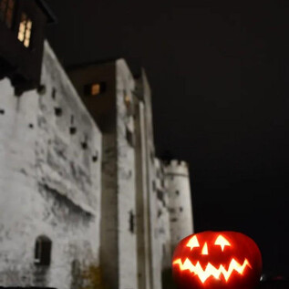 A creepy carved pumpkin glows in front of an old castle at night. The atmosphere is mysterious and fitting for Halloween. | © Salzburger Burgen und Schlösser