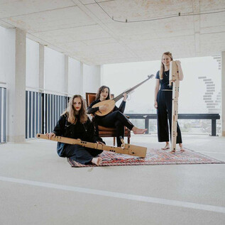 Tre musiciste sono sedute in un ambiente moderno e suonano diversi strumenti musicali. Indossano abiti neri e sembrano creative e rilassate. | © Anna Haslauer
