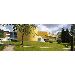 A modern building in nature, surrounded by green spaces and trees. The sky is clear and there is a sunny atmosphere. | © www.virgil.at