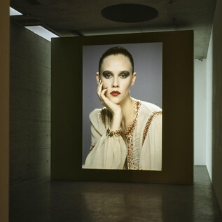 A large screen displays the portrait of a woman with striking makeup and an elegant outfit. The background is minimalist and modern. | © Generali Foundation_Margeritha Spiluttini