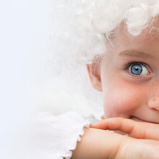 A smiling child with blue eyes and curly hair, who is leaning on their hands. The background is bright and neutral. | © Stiegl-Brauwelt