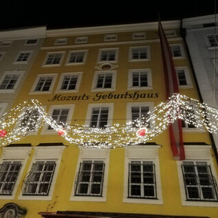A historic building known as Mozart's birthplace shines at night. The facade is adorned with festive lights and decorations. | © ISM