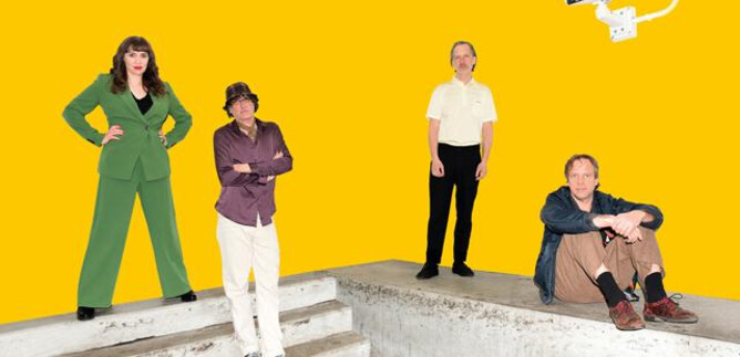 A group of four people stands on a concrete platform in front of a yellow background. They are dressed differently and posing confidently. | © Stefan Braunbarth