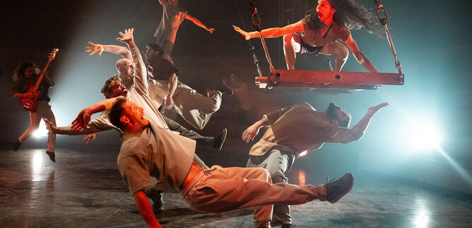 An impressive dance performance featuring multiple dancers in dynamic poses. One dancer swings on a swing while the others interact around her. | © Kalimba