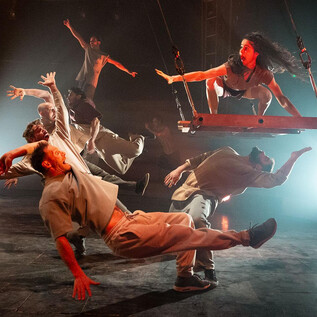 An impressive dance performance featuring multiple dancers in dynamic poses. One dancer swings on a swing while the others interact around her. | © Kalimba