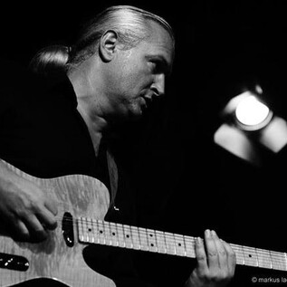 Un uomo suona la chitarra sul palco. L'atmosfera è intensa e concentrata. | © markus lackinger