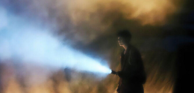A person stands in a foggy environment holding a flashlight. The light from the flashlight breaks through the fog and creates a mysterious atmosphere. | © Benjamin Blaikner