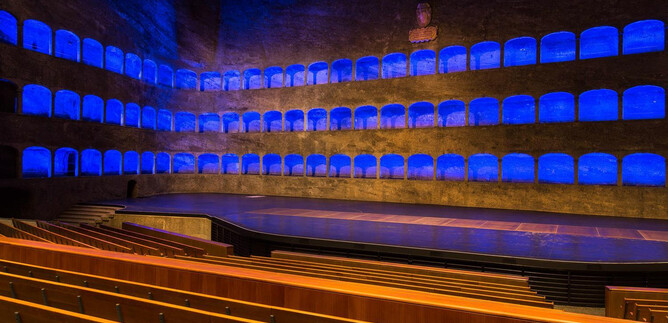 A stylish theater with blue light accents. The rows of seats are empty and the stage area is clearly visible. | © Andreas Kolarik