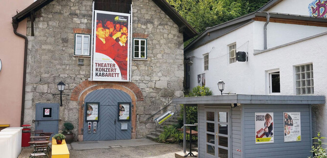 A charming theater building with a large poster wall that offers cultural events. Next door is a small kiosk with colorful advertisements. | © Kleines Theater