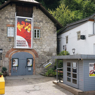 A charming theater building with a large poster wall that offers cultural events. Next door is a small kiosk with colorful advertisements. | © Kleines Theater